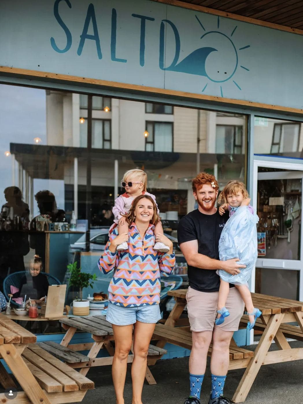 Topher and his family in front of the Saltd Surf cafe shopfront in Newquay, with the painted SALTD wave-and-sun logo above them
