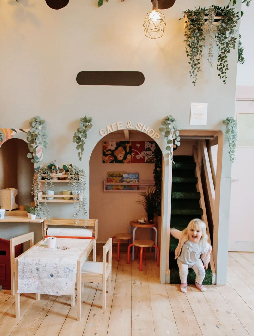 Inside Saltd — the kids' 'CAFE & SHOP' arched play space downstairs with adult seating, hanging plants and pendant light